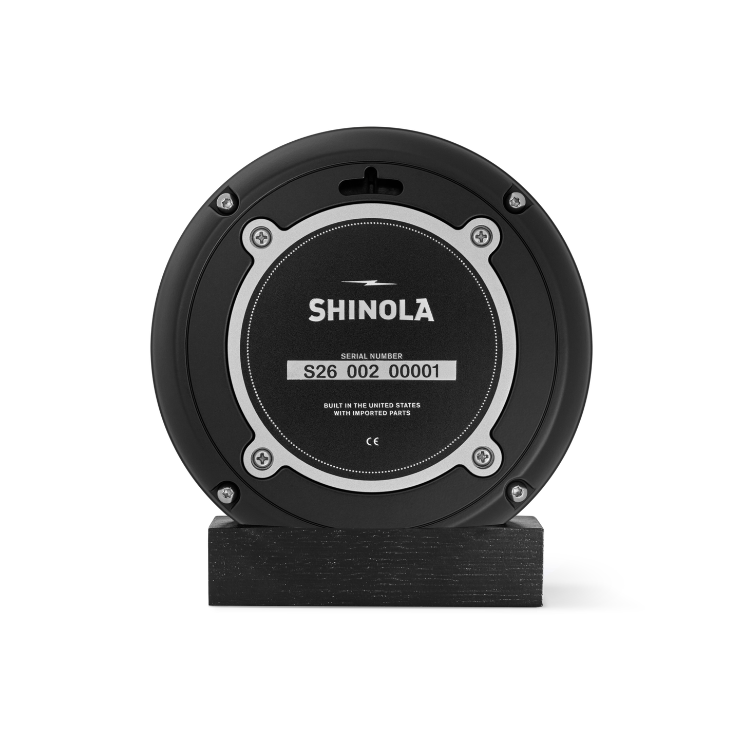 A 6" Runwell Clock - Black by Shinola, featuring a round black face with a silver-rimmed center and serial number S26 002 00001, sits upright on a rectangular black base against a white background.