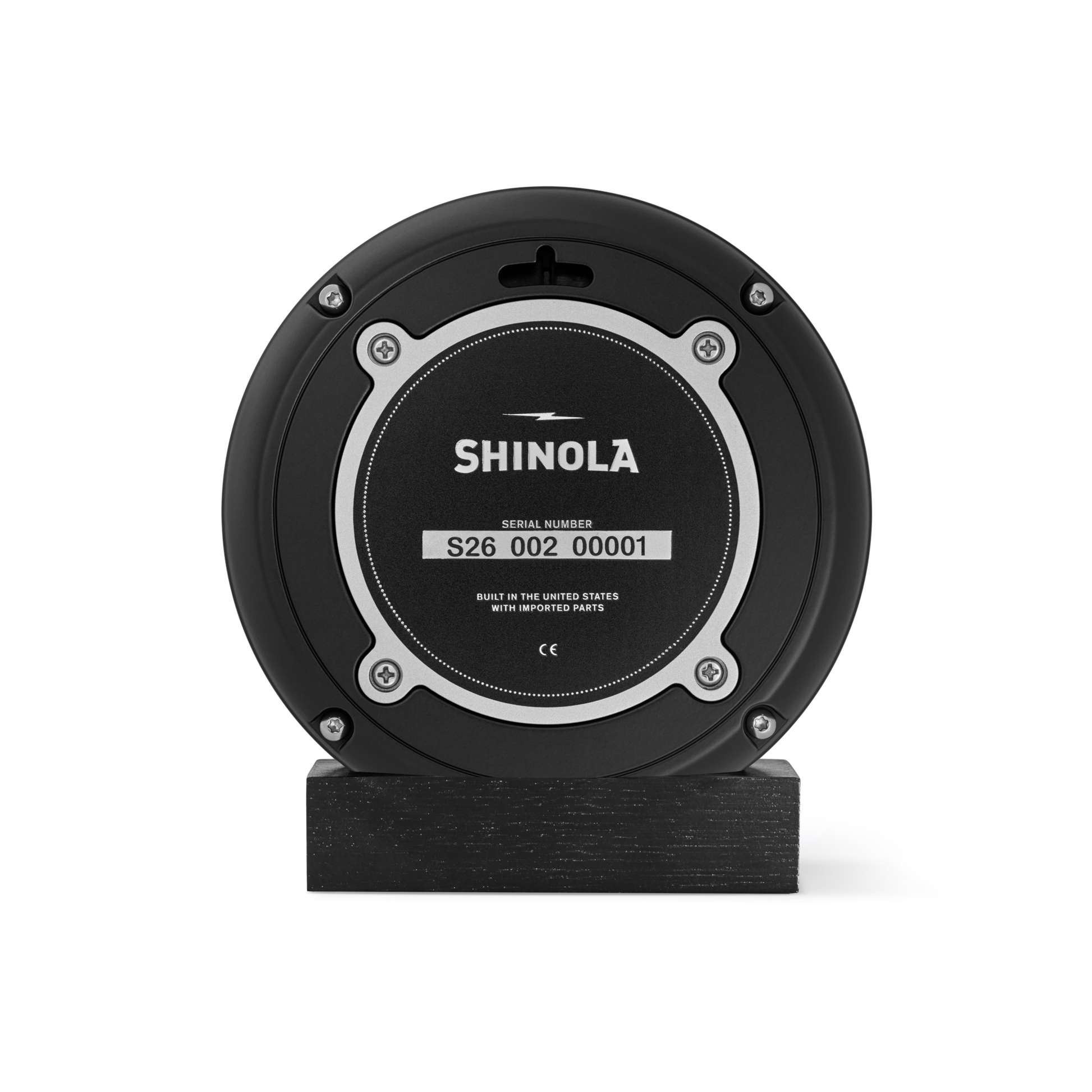 A 6" Runwell Clock - Black by Shinola, featuring a round black face with a silver-rimmed center and serial number S26 002 00001, sits upright on a rectangular black base against a white background.