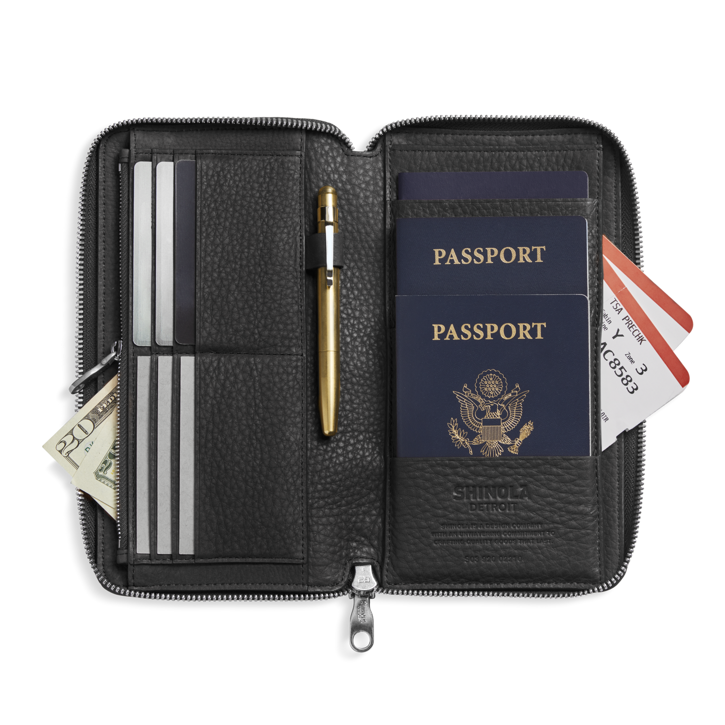 The Shinola Organizer Wallet - Black in natural grain leather opens to reveal slots for two U.S. passports, credit cards, boarding passes, a gold pen, and cash—an elegant all-in-one travel essential.