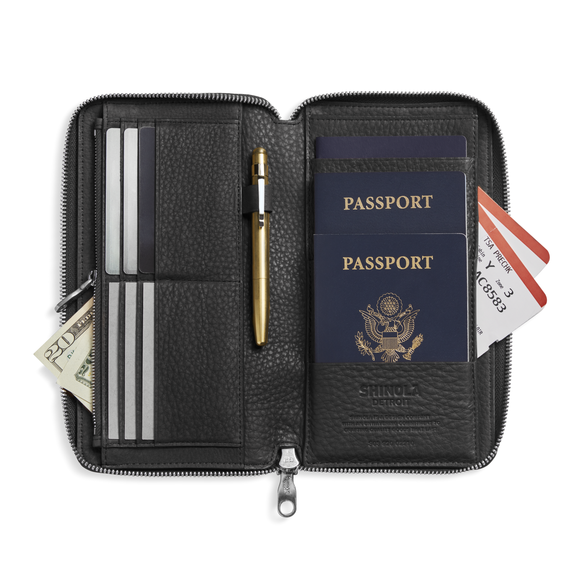 The Shinola Organizer Wallet - Black in natural grain leather opens to reveal slots for two U.S. passports, credit cards, boarding passes, a gold pen, and cash—an elegant all-in-one travel essential.