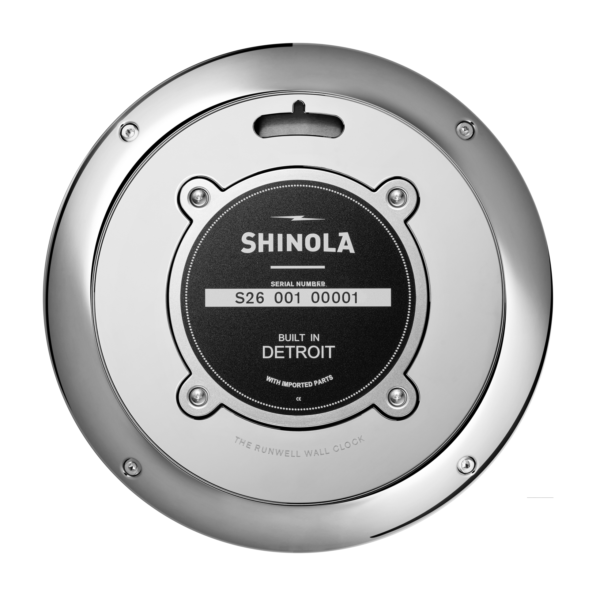 A close-up shows the back of the Shinola 14" Runwell Clock - Navy, highlighting its metallic gunmetal case and a black label with serial number S26 001 00001, reading “Built in Detroit with imported parts.”.