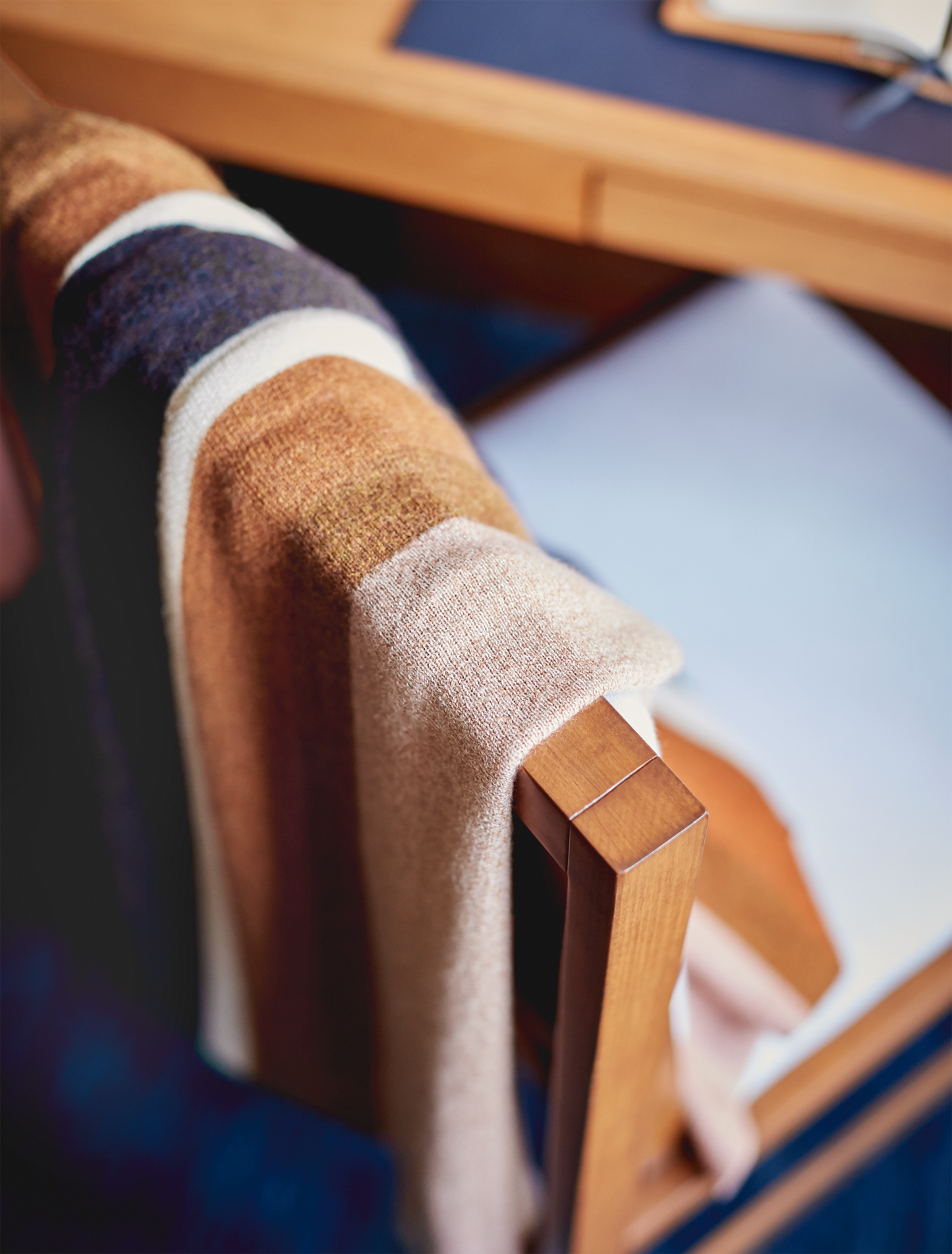 The Shinola Alpaca Throw Blanket in Pink/Beige—crafted from sustainable alpaca fiber—is draped over a wooden chair near a desk with papers and a notebook.