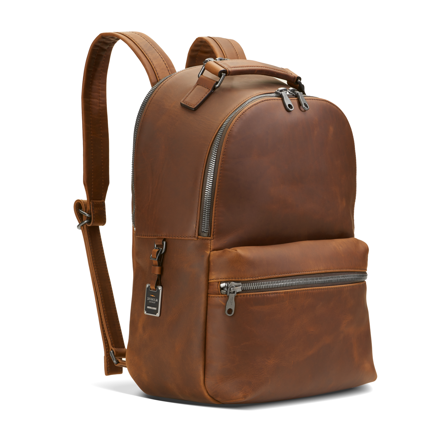 The Shinola Runwell Backpack - Medium Brown features premium natural grain leather, silver zippers, a front zip pocket, and adjustable padded straps, shown upright against a plain white background.