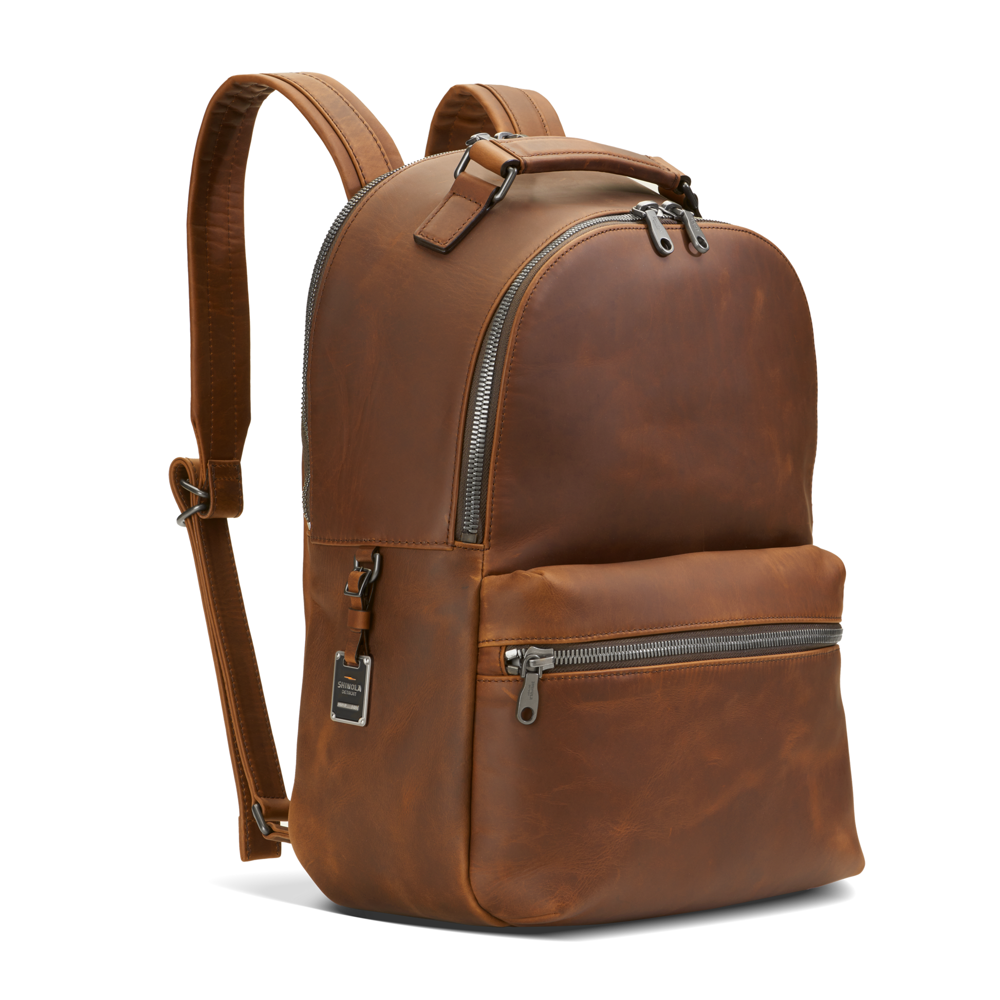 The Shinola Runwell Backpack - Medium Brown features premium natural grain leather, silver zippers, a front zip pocket, and adjustable padded straps, shown upright against a plain white background.