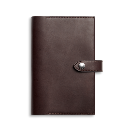 The Shinola Medium Journal Cover in dark brown Italian leather features a closed design with a buttoned strap closure, shown against a plain white background.
