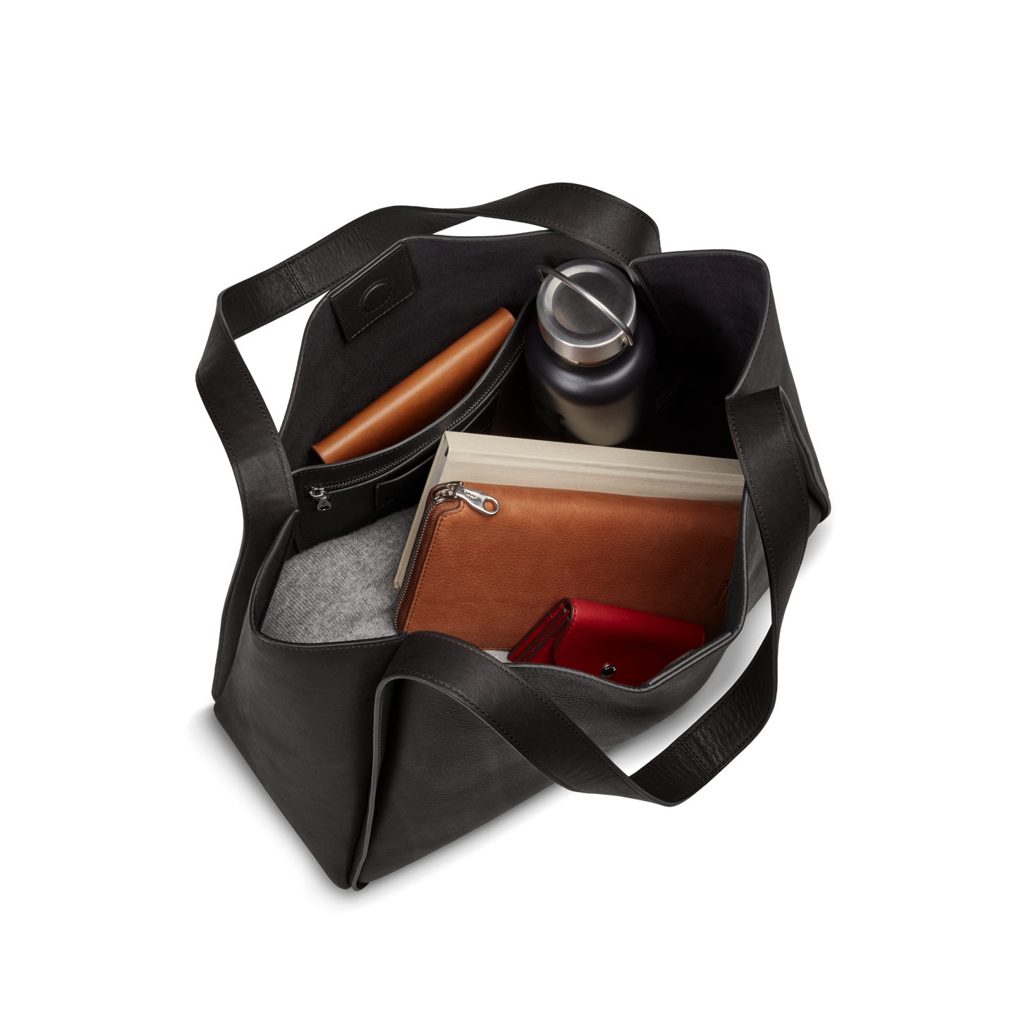 The Shinola Derby Tote Bag - Black, crafted from natural leather, holds a laptop, water bottle, brown pouch, red wallet, grey felt case, and notebook—ideal as your versatile everyday bag with all items visible from a top-down view.