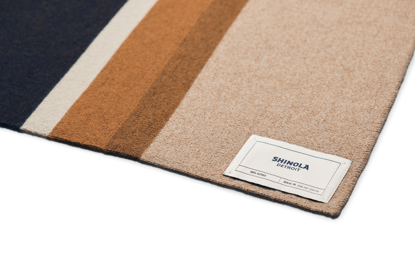 A close-up of the Shinola Alpaca Throw Blanket in Pink / Beige, showing its soft fabric with wide vertical stripes and a sewn-on brand label—crafted from sustainable alpaca fiber for a luxurious feel.